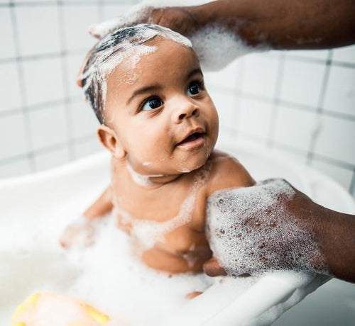 Un bebé disfruta de un baño de burbujas mientras su papá le limpia la cabeza con shampoo Mustela - Mustela España - 1