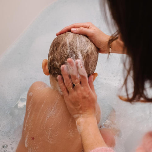 Una mamá limpia la cabeza de su bebé con champú Mustela mientras él disfruta de un baño de espuma - Mustela España - 1
