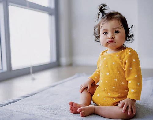 Una niña con piel atópica está sentada en un alfombra - Mustela España - 1