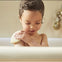 Una niña de 3 años usa el champú sólido 2-en-1 Mustela para lavarse el cuerpo en la bañera. slider