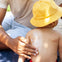 un padre aplica protector solar en la espalda de su niño que lleva un gorro. slider