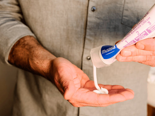 Un papá se dosifica en la mano la crema bálsamo 123 de Mustela para picores y rojeces antes de aplicarlo en la zona del pañal de su bebé - Mustela España - 6