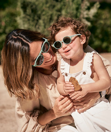 Madre e hija disfrutan de un día de paseo en verano con los ojos protegidos gracias a las gafas de sol Bebé Aguacate de color verde de Mustela.