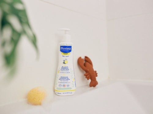 Bote de gel hidratante para bebés con piel seca en una repisa del baño familiar junto una esponja - Mustela España - 5