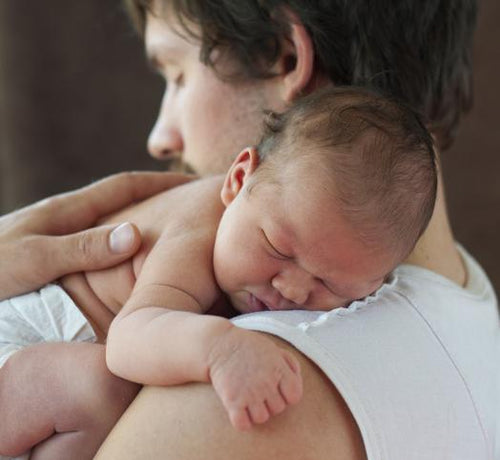 Hombre joven con su bebé dormido a cuestas después de un baño relajante con productos Mustela - Mustela España - 1