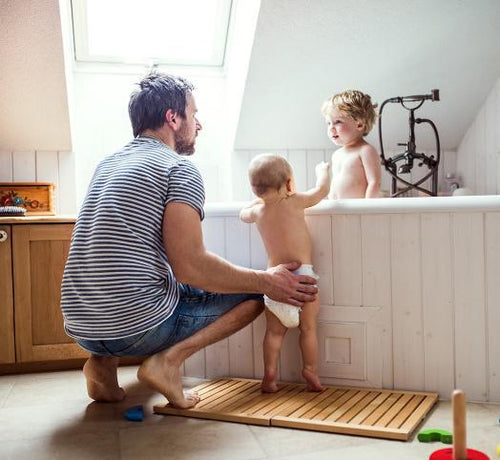 Un papá a punto de dar un baño relajante a sus dos hijos, uno de ellos todavía bebé, con productos para la higiene Mustela - Mustela España - 1