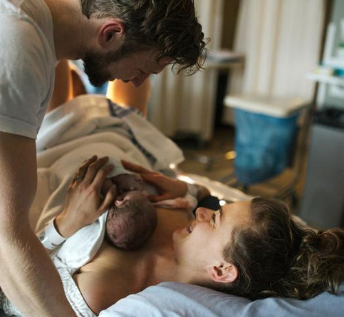 Una mujer y un hombre se sonríen momentos después del parto al ver a su bebé. - Mustela España - 1