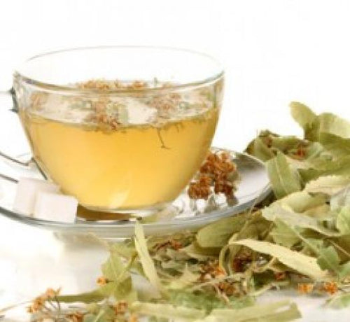 Una taza con infusión de tila, un par de azucarillos y rodeada de hojas de tilo - Mustela España - 1