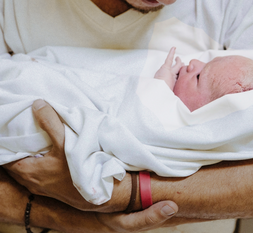 Papá cogiendo a su bebé recién nacido sobre una toalla blanca. - Mustela España - 1