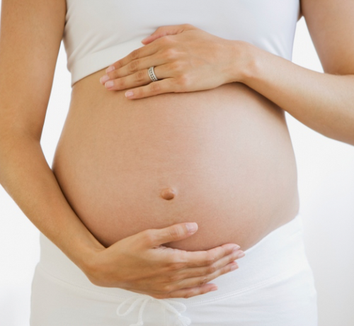 Plano de una tripa de una mamá vestida con pantalon blanco y toop blanco mientras abraza su tripa con las manos. - Mustela España - 1