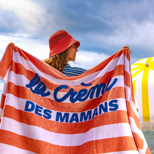 Una mujer sujetando su toalla en el playa. La toalla tiene la frase "la créme de mamans" - Mustela España - 1