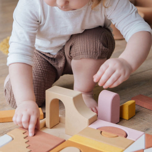 Niña pequeño jugando con bloques de madera de colores durante una actividad educativa en el suelo. - Mustela España - 1