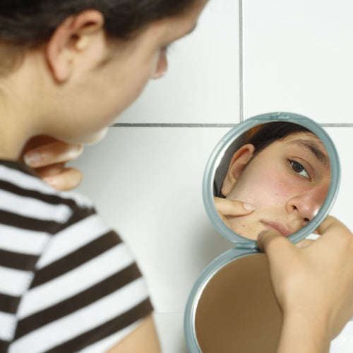 Mujer viendose las manchas de embarazo en la piel de si rostro con un espejo de mano. - Mustela España - 1