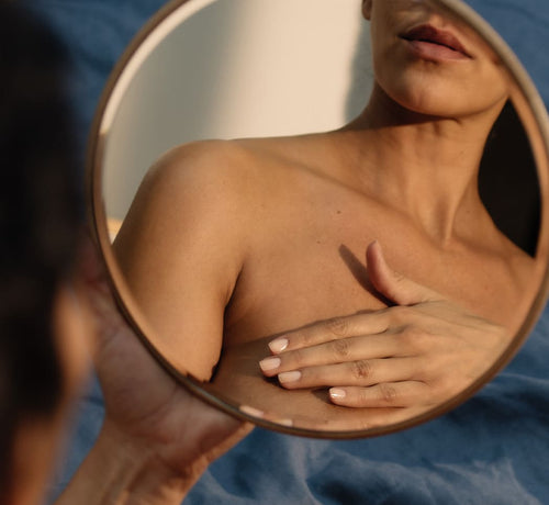 Mujer frente a un espejo redondo aplicándose una crema antiestrías en el pecho - Mustela España - 1