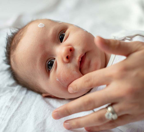 Mujer aplicando con la mano crema sobre la piel de un recién nacido con piel atópica. - Mustela España - 1