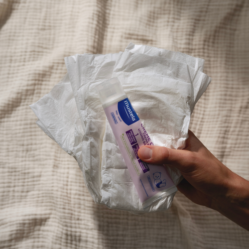 Mano sujetando la Crema bálsamo 1 2 3 de Mustela sobre unos pañales. - Mustela España - 1