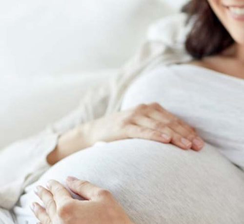 Una mujer embarazada feliz mientras se acaricia la barriga durante los últimos meses de gestación - Mustela España - 1