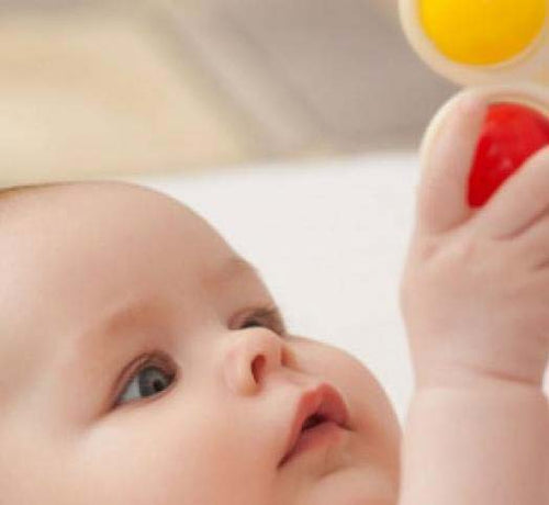 Un bebé juega con sus juguetes mientras está estirado en su cunita - Mustela España - 1