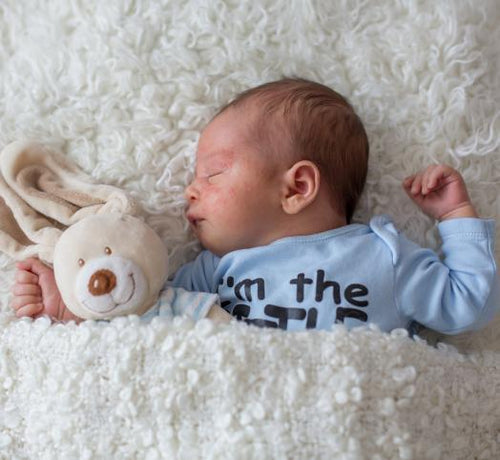 Bebé durmiendo plácidamente arropado sobre una sabana blanca y con un osito de peluche. - Mustela España - 1