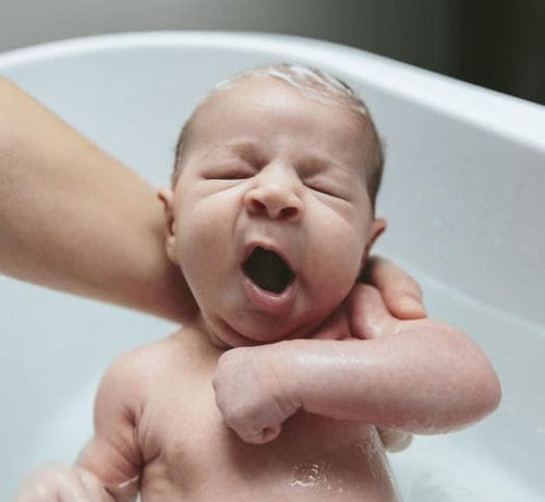 Un bebé en los brazos de su mamá mientras recibe un baño de espuma con productos Mustela - Mustela España - 1