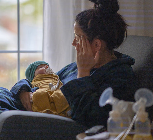 Mama sentada sobre un sillón cogiendo a su bebé mientras le mira fijamente. - Mustela España - 1