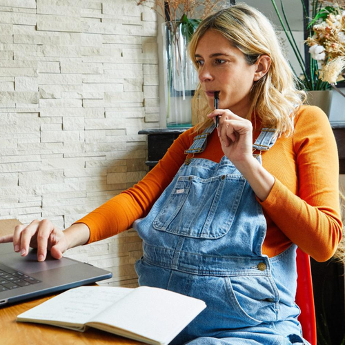 mujer embarazada pensando frente a su portátil para anotar cosas - Mustela España - 1