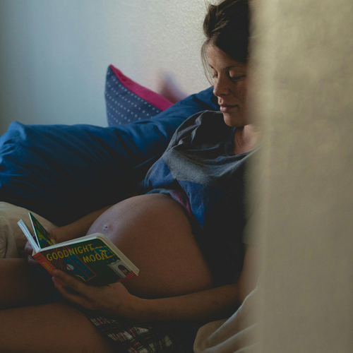 Mujer embarazada sentada en un sillón mientras ve un libro para bebés. - Mustela España - 1
