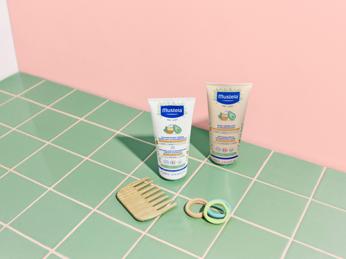 Nuevo champú y acondicionador de Mustela sobre azulejos verdes con un peine y tres coletas para el pelo de colores. - Mustela España - 3