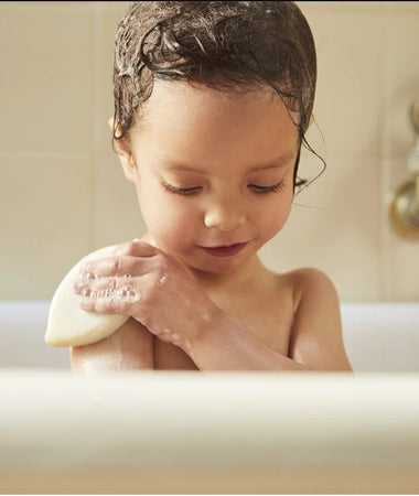 Una niña de 3 años usa el champú sólido 2-en-1 Mustela para lavarse el cuerpo en la bañera. 