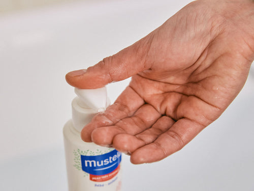 Madre se pone un poco de gel de baño confort en la mano lavar la piel sensible de su bebé. - Mustela España - 3