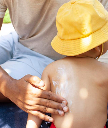 un padre aplica protector solar en la espalda de su niño que lleva un gorro. 