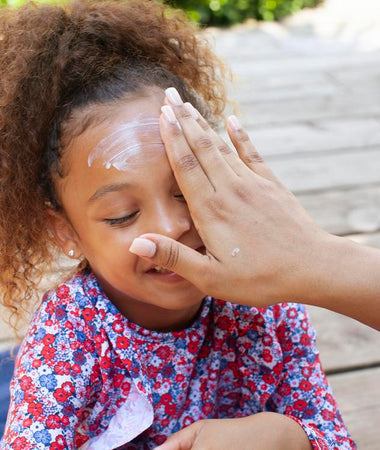 Una madre aplica crema solar en la cara de su niña. 