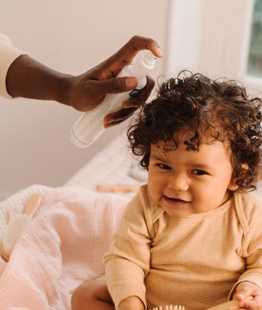 Una padre usa el Agua para peinar de Mustela en el pelo de su niña con pelo rizado. 