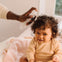 Una padre usa el Agua para peinar de Mustela en el pelo de su niña con pelo rizado. slider
