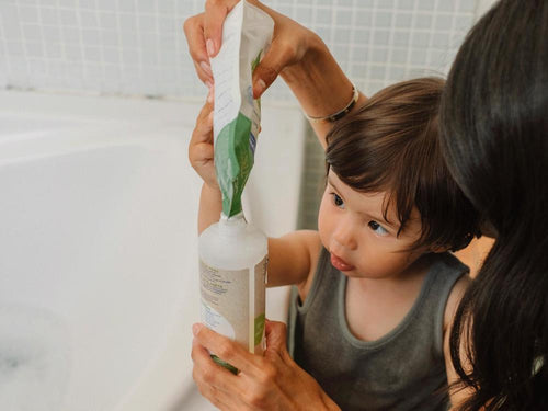 Un niño con su madre está rellenando el envase del gel-champú bio de Mustela con su eco-recarga. slider - Mustela España - 4
