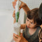 Un niño con su madre está rellenando el envase del gel-champú bio de Mustela con su eco-recarga. slider
