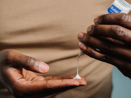 Padre se aplica un poco de crema Mustela para cuidar la costra láctea de su bebé en los dedos. slider - Mustela España - 2