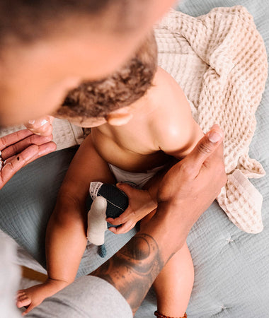Padre aplica la crema bálsamo emoliente en la piel con dermatitis atópica de su bebé, después del baño. 