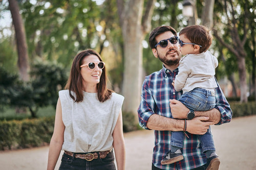Una familia joven, compuesta por una madre, padre y un bebé, disfruta de un paseo por un parque, llevan gafas Mustela by Parafina en diferentes modelos.slider - Mustela España - 2