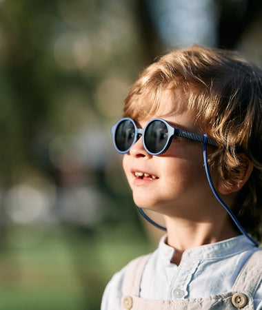 Bebé entre 1 y 2 años disfruta de un día soleado en el parque con las gafas de sol aguacate de Mustela by Parafina en color azul.