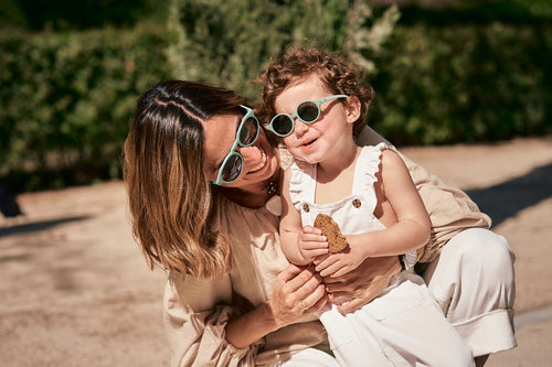 Madre e hija disfrutan de un día de paseo en verano con los ojos protegidos gracias a las gafas de sol Bebé Aguacate de color verde de Mustela.slider - Mustela España - 3